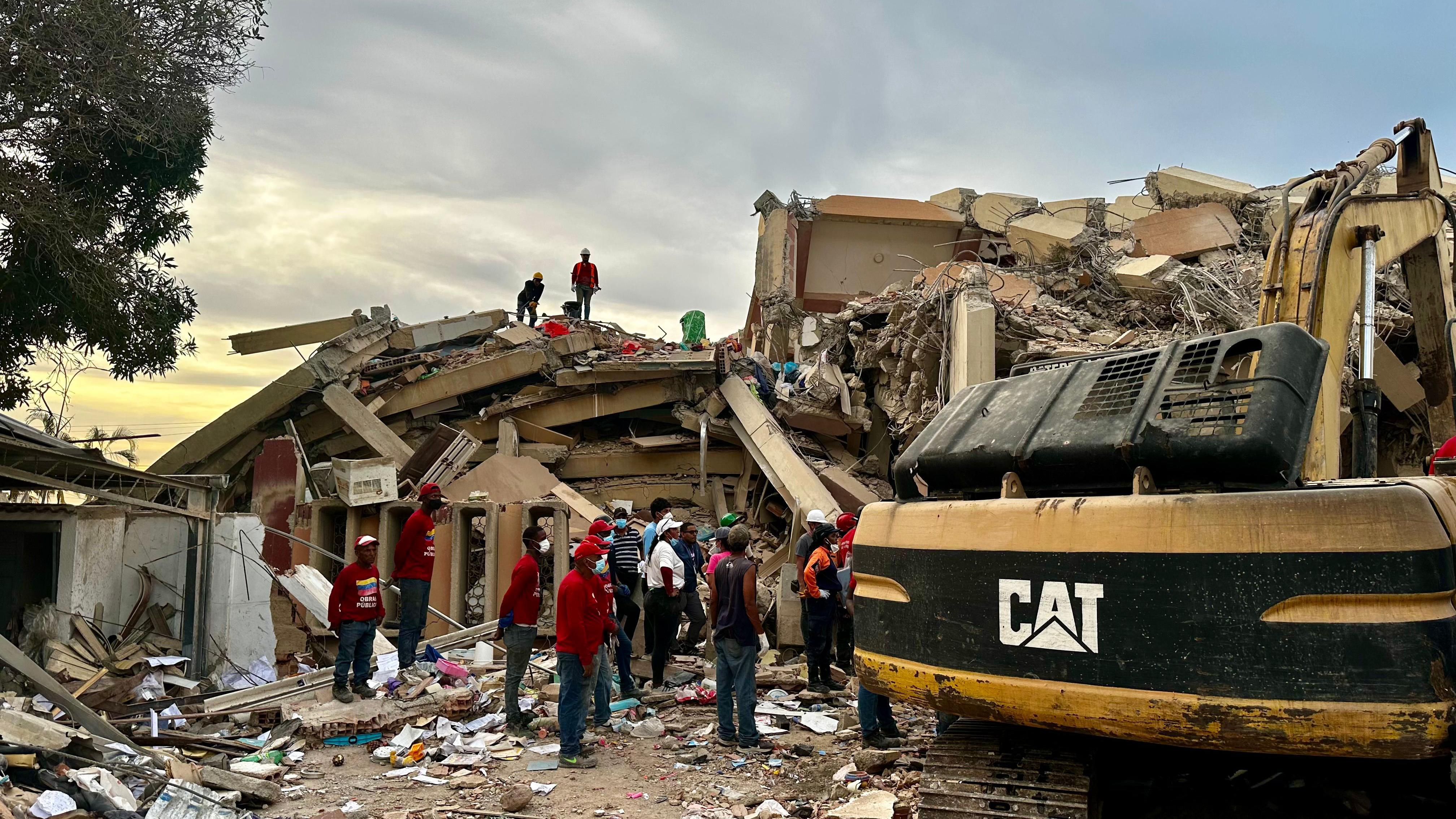 Rescatistas trabajando al atardecer para remover los escombros del conjunto residencial. Hay una grúa a un lado de ellos.