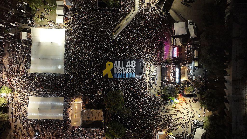 مشهد من الأعلى ليلاً، لآلاف المتظاهرين في تل أبيب، وتظهر لافتة مكتوب عليها باللغة الإنجليزية "أعيدوا كل الـ 48 رهينة إلى بيوتهم الآن".
