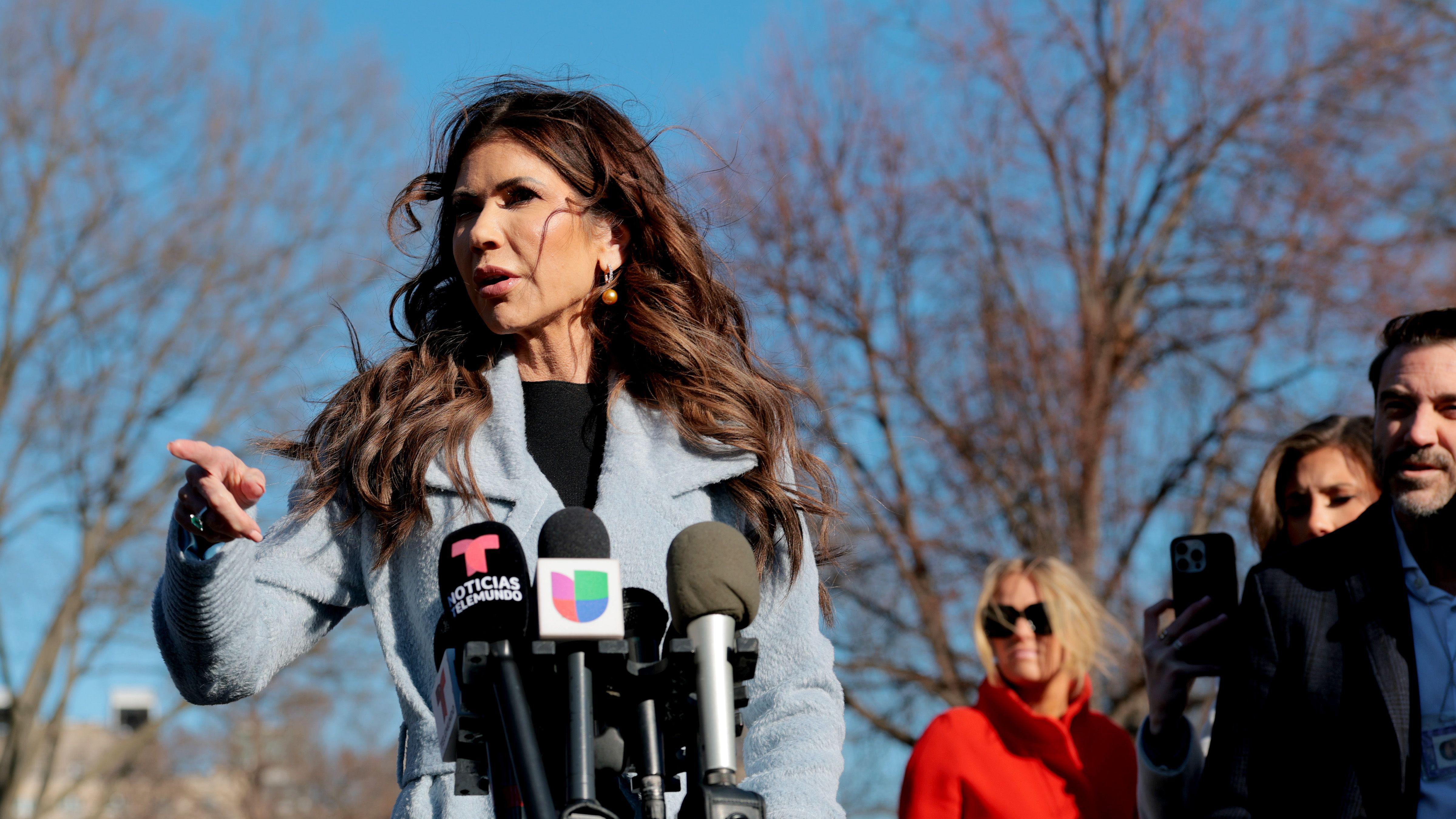 Kristi Noem señala con su índice derecho mientras habla ante los periodistas en un espacio exterior en Washington DC.