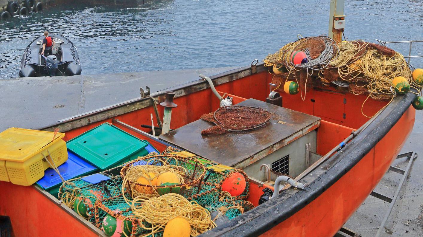 Barco de pesca carregado de redes e pronto para zarpar, com lancha rebocadora.