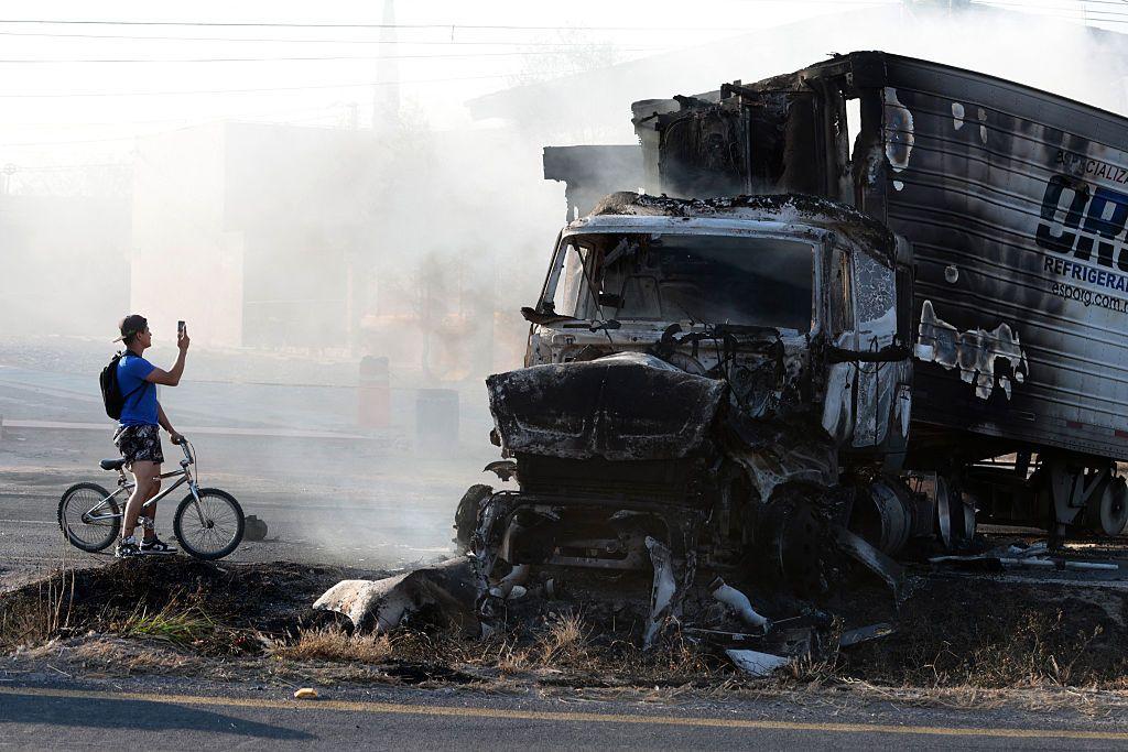 Un hombre en bicicleta toma una foto junto a un camión incendiado en Jalisco