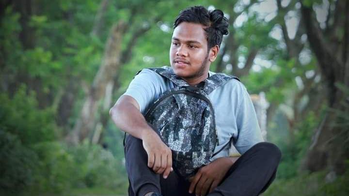 畫面中可以看到一位黑髮青年背著背包坐在樹前。