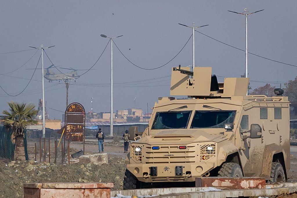 دبابة عسكرية وفي الخلفية اثنان يمشيان وفي السماء تظهر طائرة عسكرية أمريكية. 