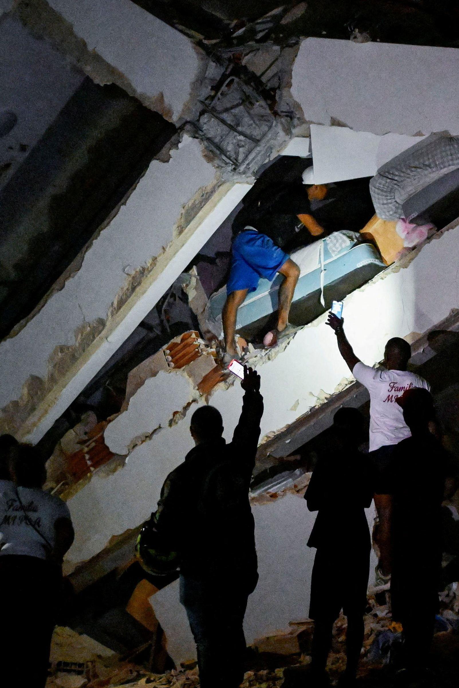 Hombre busca sobreviviente en los escombros y otros alumbran con sus celulares en La Guaira, Venezuela.