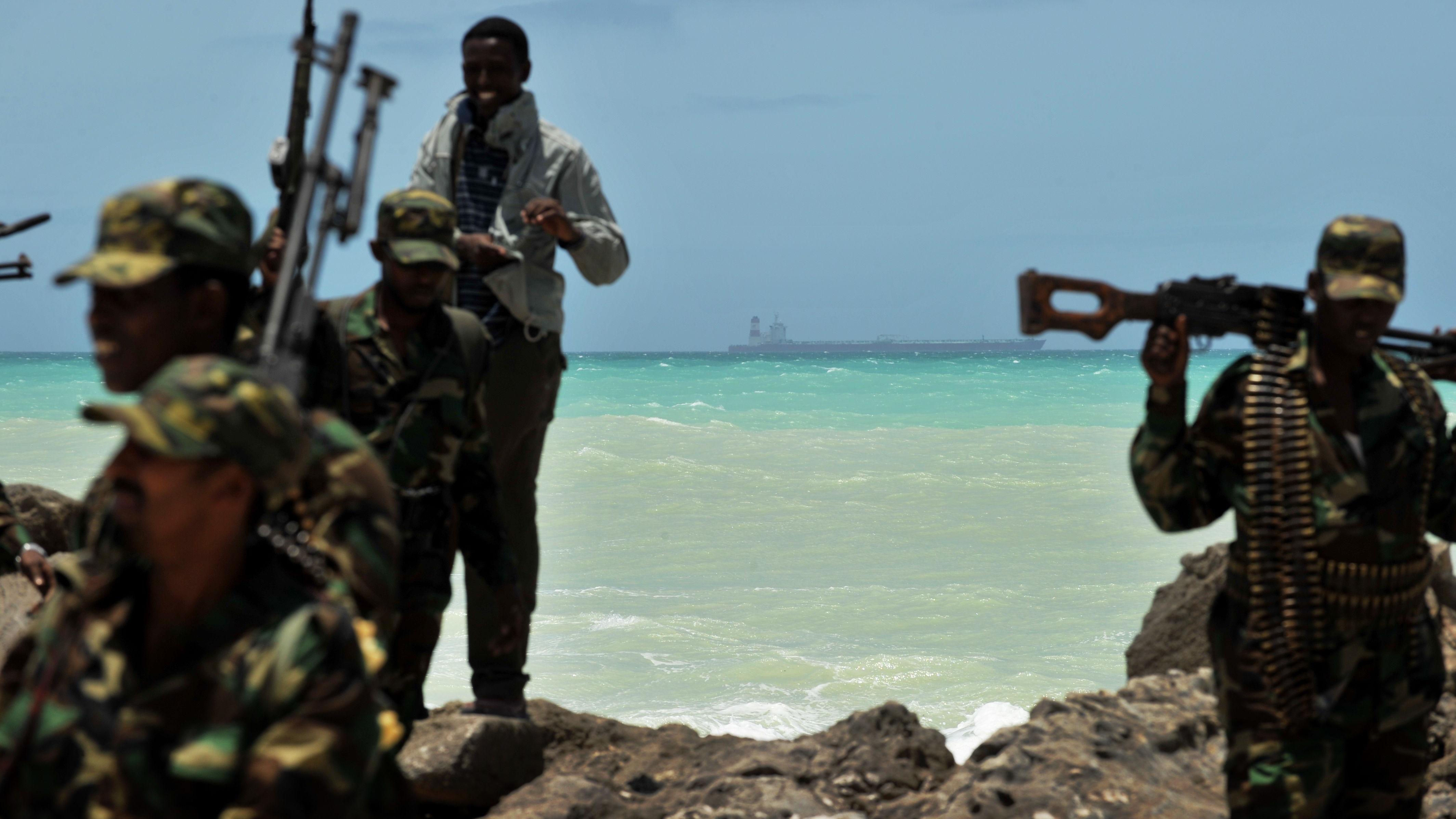 Miembros de una milicia armada y un pirata caminan sobre una formación rocosa en la localidad somalí de Hobyo, mientras en el horizonte se observa un superpetrolero secuestrado anclado el 20 de agosto de 2010.