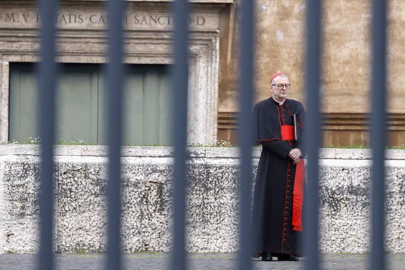 Cardeal católico de pé atrás de uma grade, em frente a um santuário