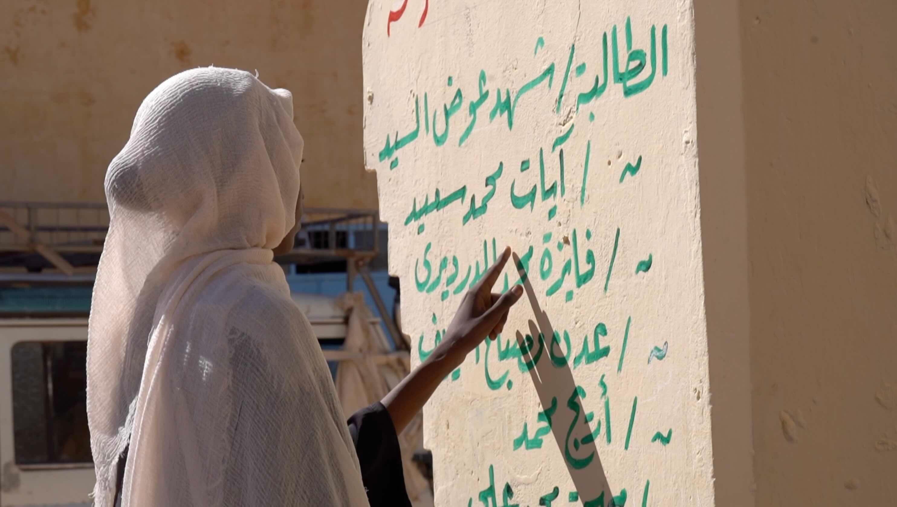 مكارم أمام جدار كُتب عليه أسماء الطالبات اللاتي قتلن في الهجوم.