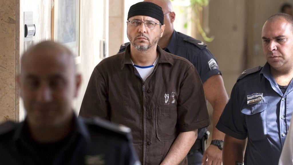 البرغوثي بلباس السجن البني تقتاده شرطة إسرائيلية، ويرتدي قبعة سوداء على رأسه.