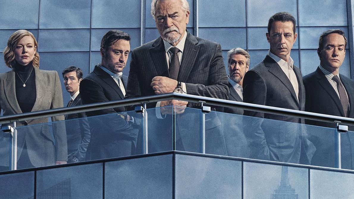 Los actores de la serie de televisión Succession, aparecen en la terraza de un moderno edificio de cristal. En primer plano está el padre, y detrás están sus hijos y otros miembros de la familia ficticia.