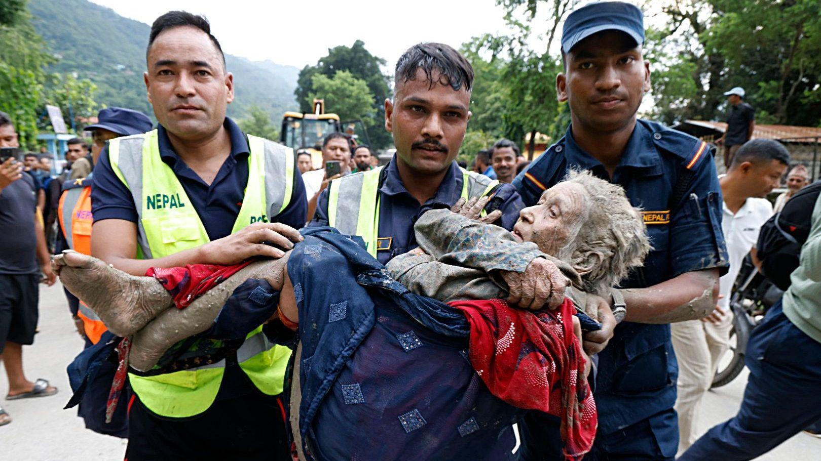 Rescatistas cargan a una anciana cubierta de barro en Nepal.