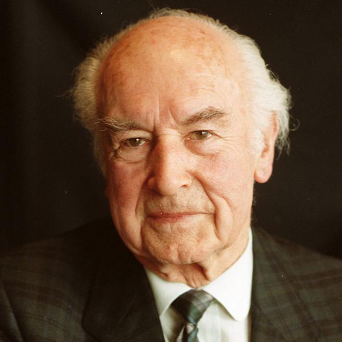 O cientista su&iacute;&ccedil;o Albert Hofmann, de terno e gravata, sorrindo para a c&acirc;mera.