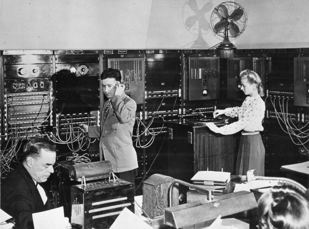 Vista de los operadores en la sala de control de Muzak, Nueva York, 1950. Supervisaban los programas de música de fondo y realizaban ajustes mediante un sistema similar a una central telefónica.
