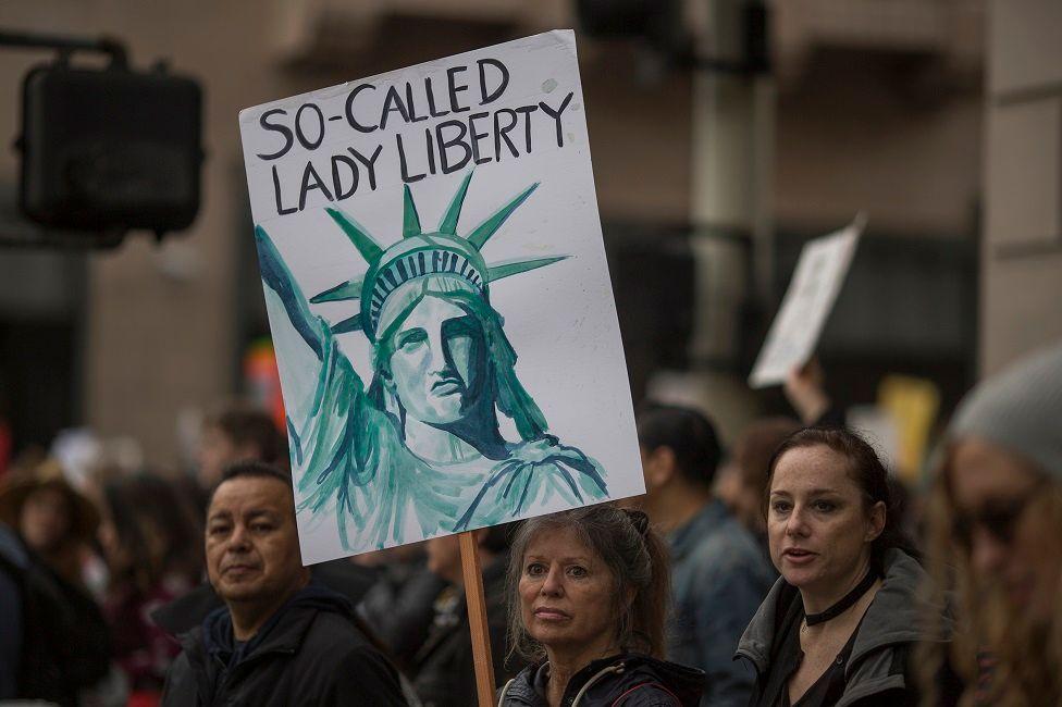 Una mujer con una pancarta en la que está dibujada la estatua de la libertad y dice: "La llamada dama libertad".