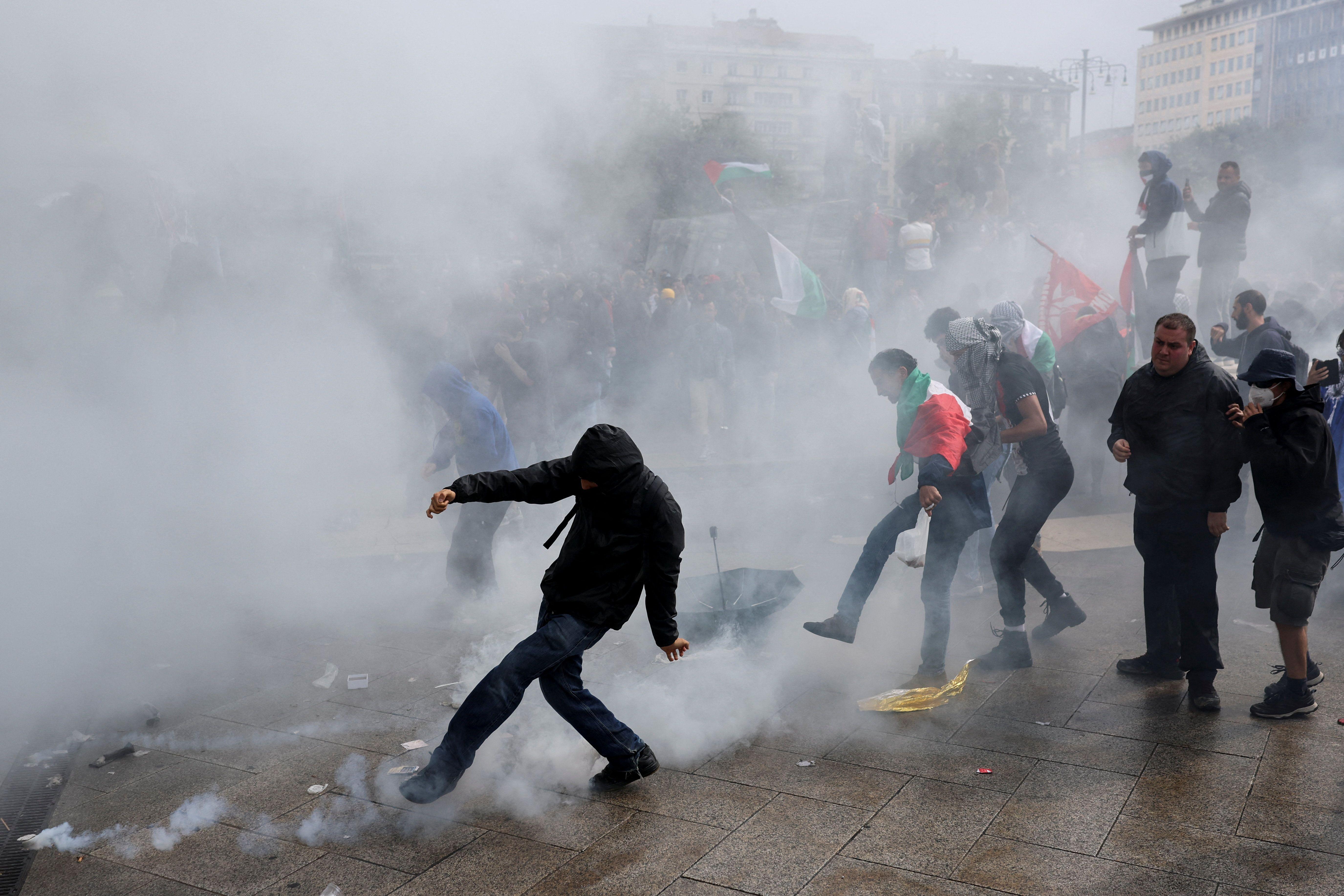 صورة تظهر انتشار الغاز المسيل للدموع في أحد الشوارع التي تشهد مظاهرات في إيطاليا، أحد المتظاهرين يرتدي علماً فلسطينياً