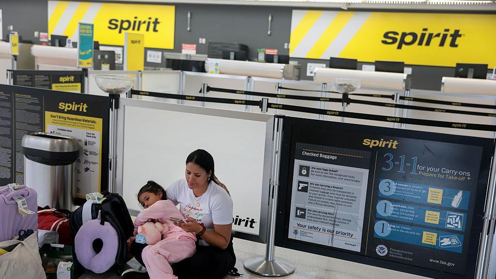 Una mujer colombiana con su hija de brazos, sentada en el counter vacío de Spirit Airlines