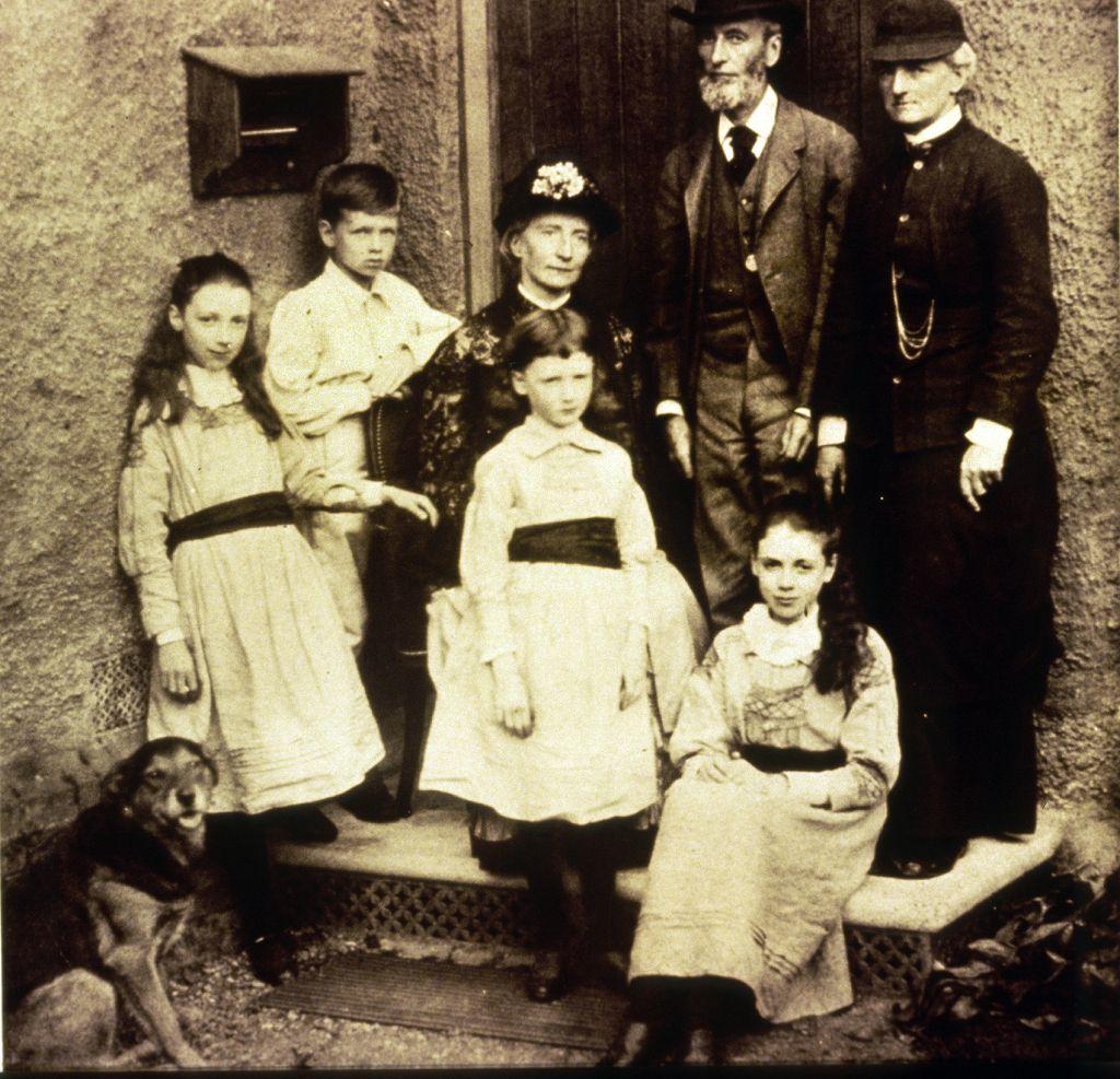 Eglantyne sentada en el escalón de la entrada de la casa con su tía y familiares