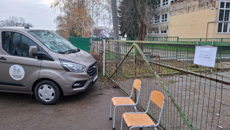 kombi stoji ispred kapije škole u mađarskom selu, dve stolice su pored 