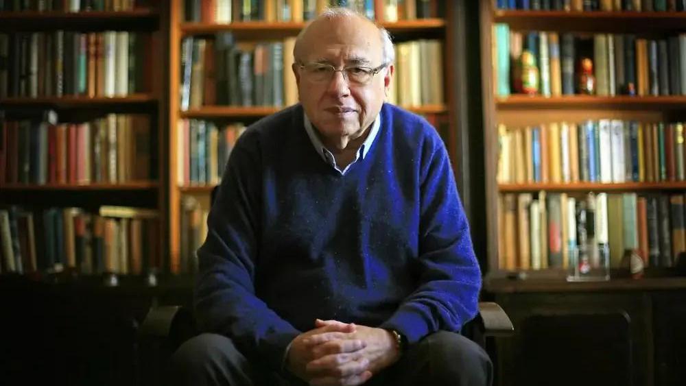 Luis Fernando Verissimo sentado em frente a uma estante de livros.