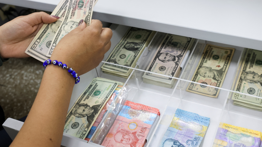 Una mujer con una pulsera azul cuenta dólares de un cajón abierto.