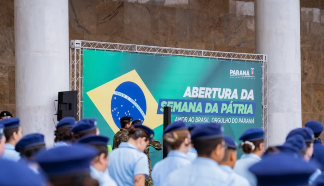 Estudantes de uniforme em escola cívico-militar do Paraná, com placa do programa ao fundo e bandeira do Brasil