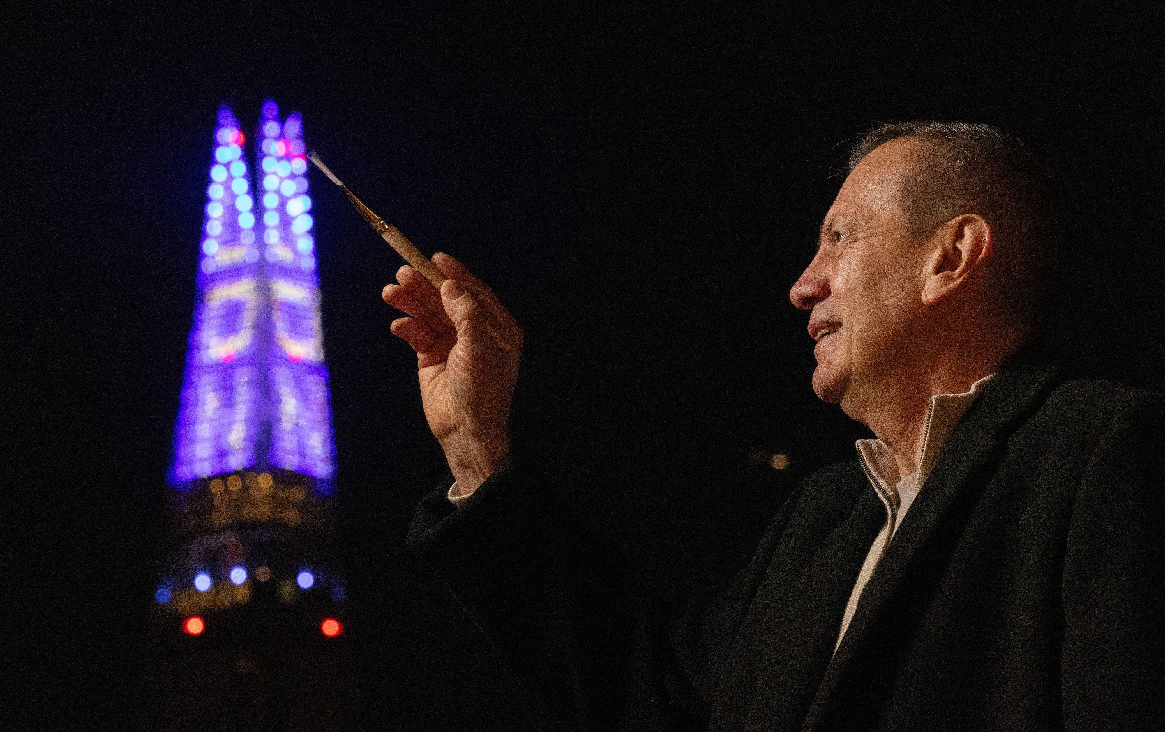 Una imagen del pintor Gustavo Zuluaga con un pincel en la mano apuntando a la torre The Shard, que se ve iluminada en el fondo de la foto.