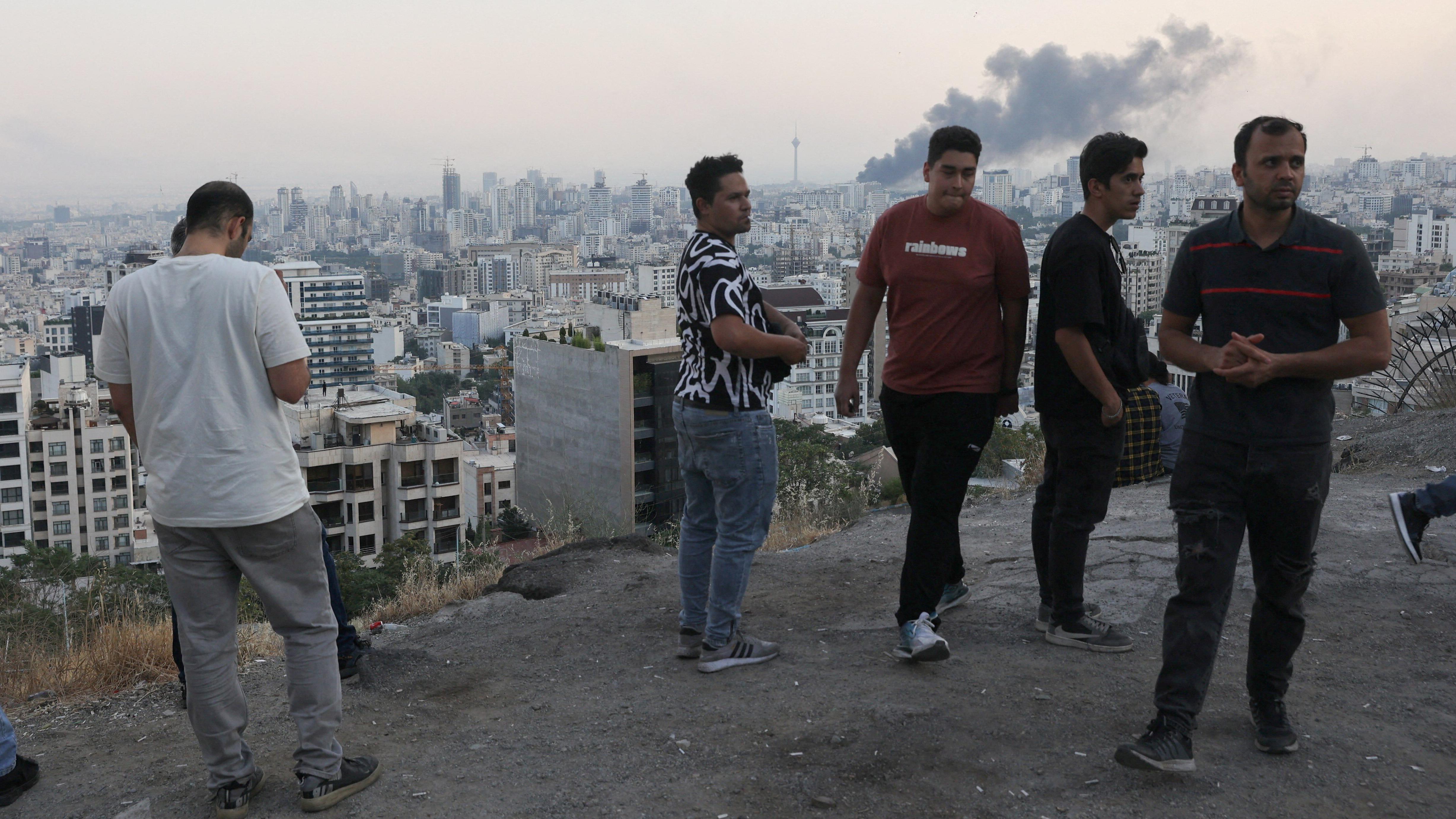Varios hombres observan desde una colina el humo que sale de la emisora estatal iraní tras ser bombardeada por Israel.