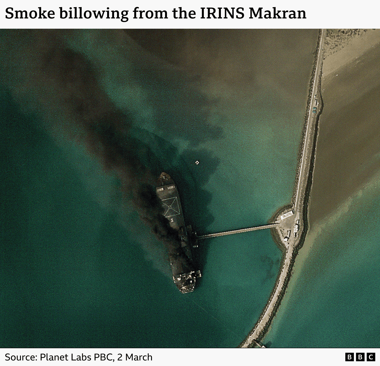 A satellite image showing an Iranian ship ablaze in a port. The caption reads "Smoke billowing from the IRINS Makran.