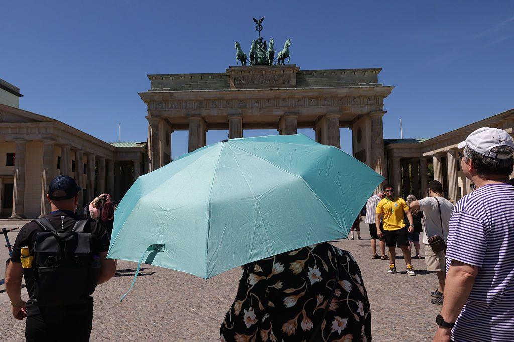 Turistas, uno de ellos bajo una sombrilla, frente a la Puerta de Brandeburgo, en Berlín, durante un día soleado.