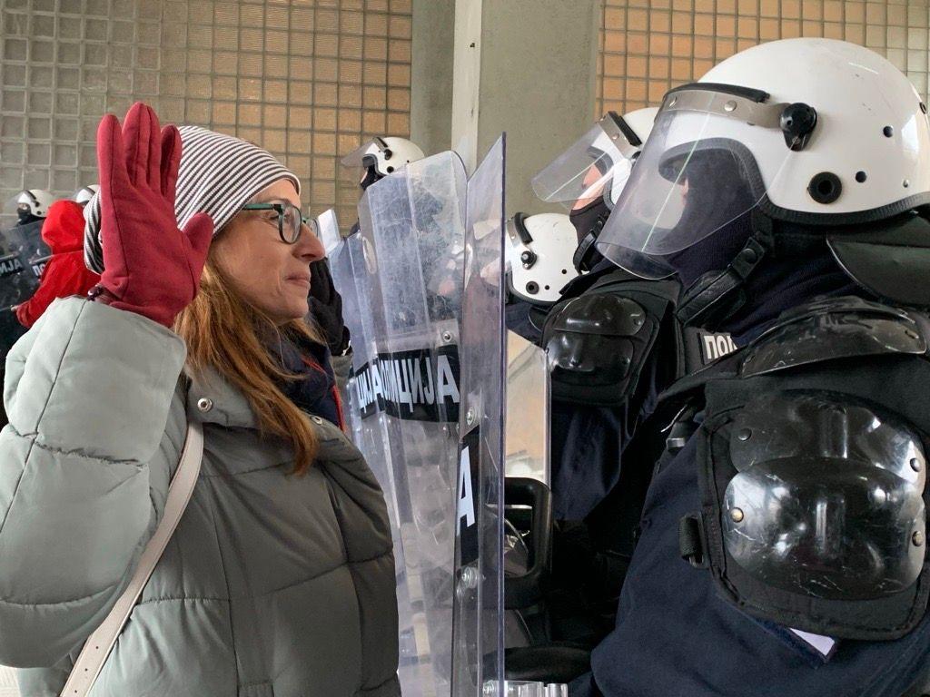 Žena sa podignutim rukama ispred policajca pod punom opremom za razbijanje demonstracija