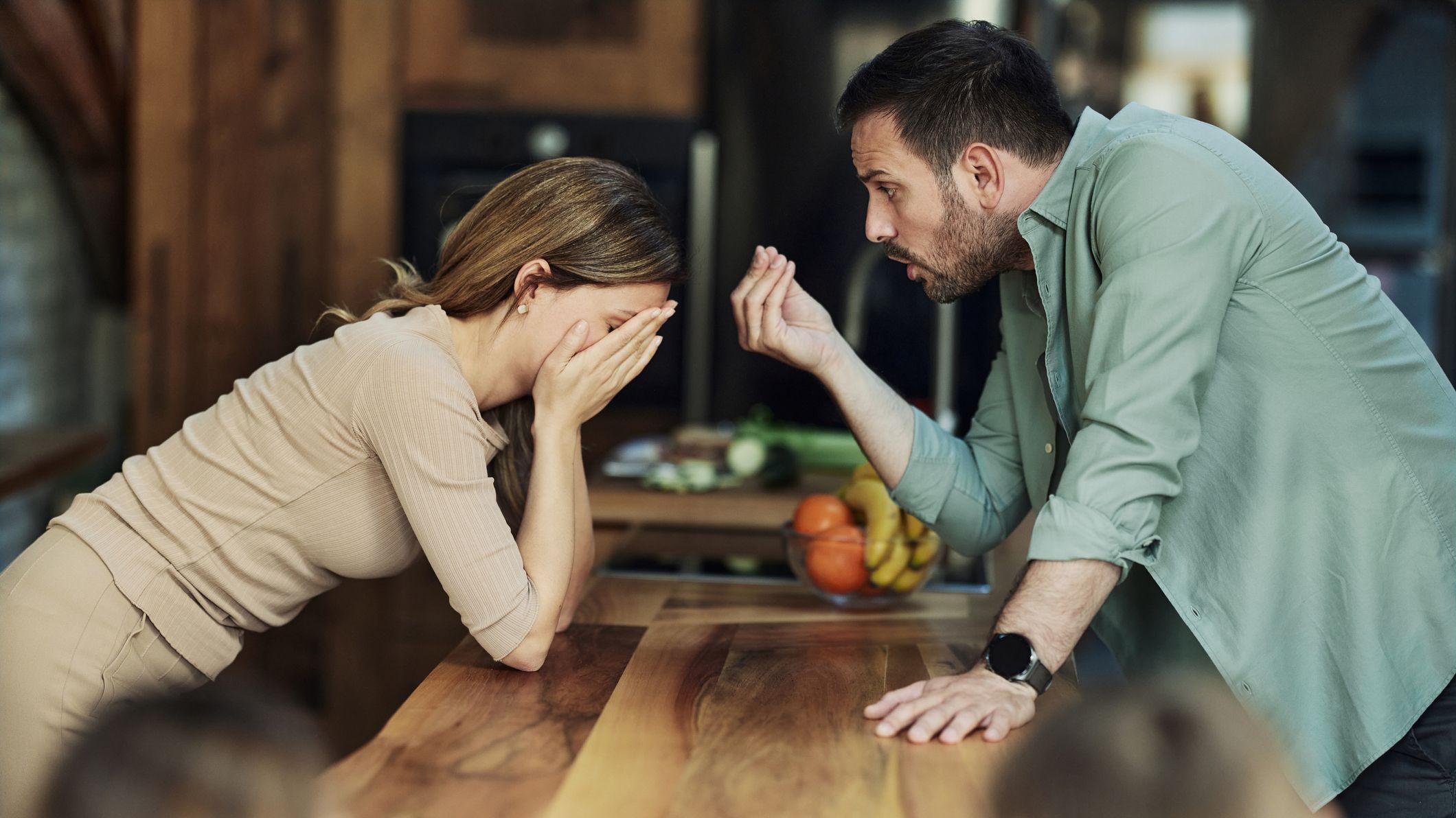 Una mujer apoya los codos sobre una mesa y se tapa la cara mientras un hombre gesticula hablándole. 