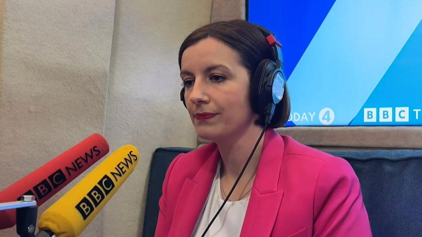 MInistra con dos micrófonos de la BBC delante.