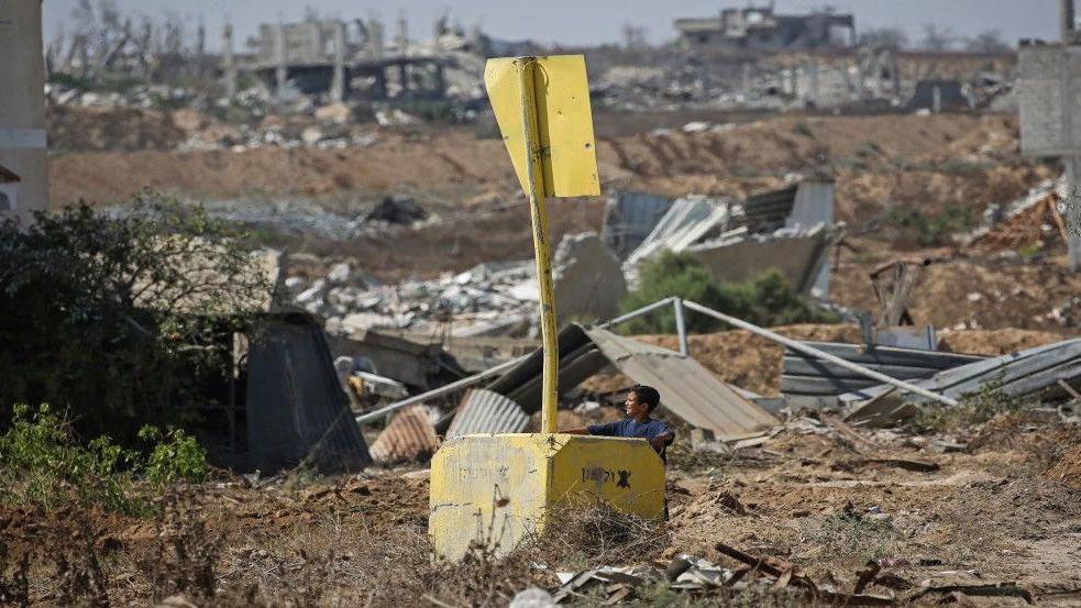 طفل يتكئ على كتلة خرسانية تحمل لافتة تدل على الخط الأصفر بينما ينظر للبعيد 