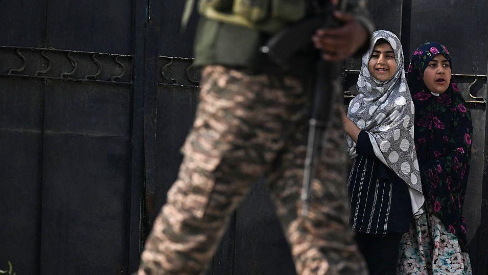 Seorang personel keamanan India (kiri) berjaga saat warga menyaksikan di Wuyan, dekat kota utama Srinagar di Kashmir yang dikuasai India, pada 7 Mei 2025.