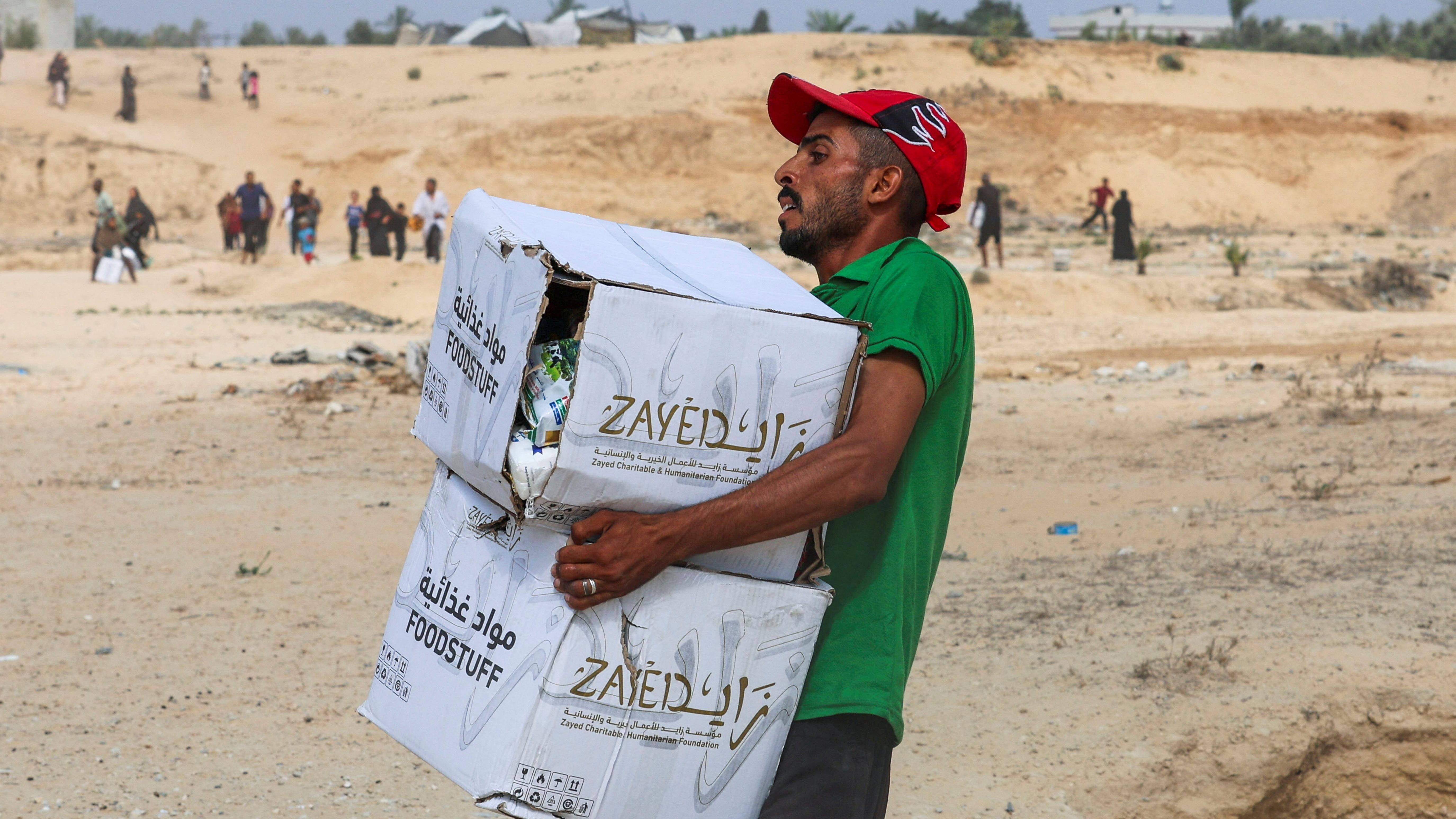 رجل فلسطيني يحمل مواد غذائية جُمعت من طرود مساعدات أُلقيت من طائرة، وسط أزمة جوع، في دير البلح وسط قطاع غزة.