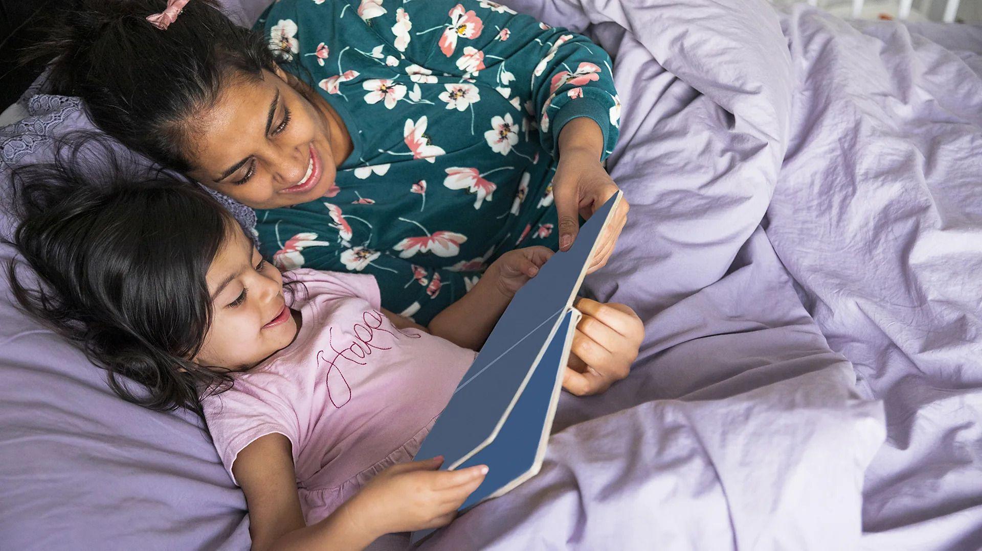 Dve devojčice leže u pidžamama i listaju knjigu