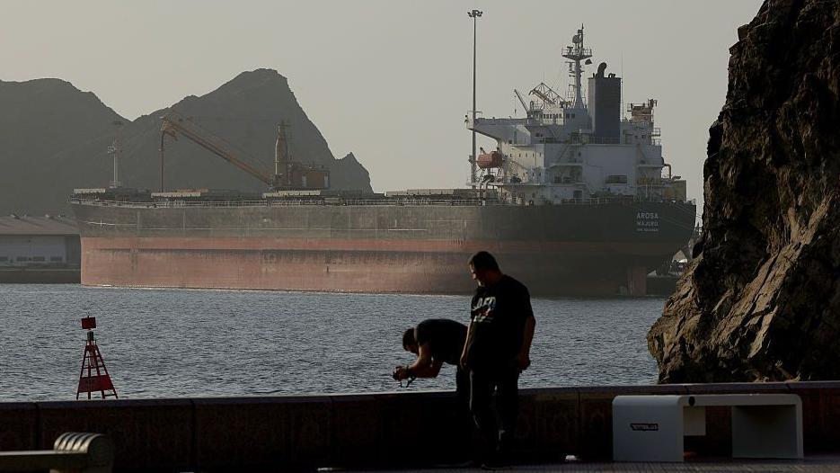 Unos hombres fotografían un barco tanquero que está en el golfo de Omán a la espera de cruzar el estrecho de Ormuz.