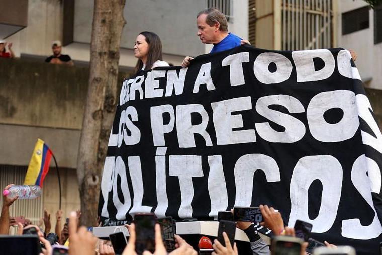 Líderes da oposição venezuelana, María Corina Machado e Juan Pablo Guanipa seguram faixa pedindo a liberdade dos presos políticos no país