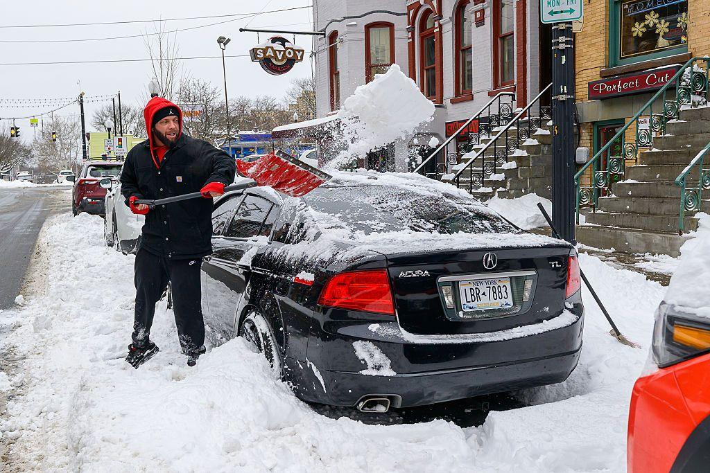 Un hombre quita la nieve alrededor de un auto en Albany