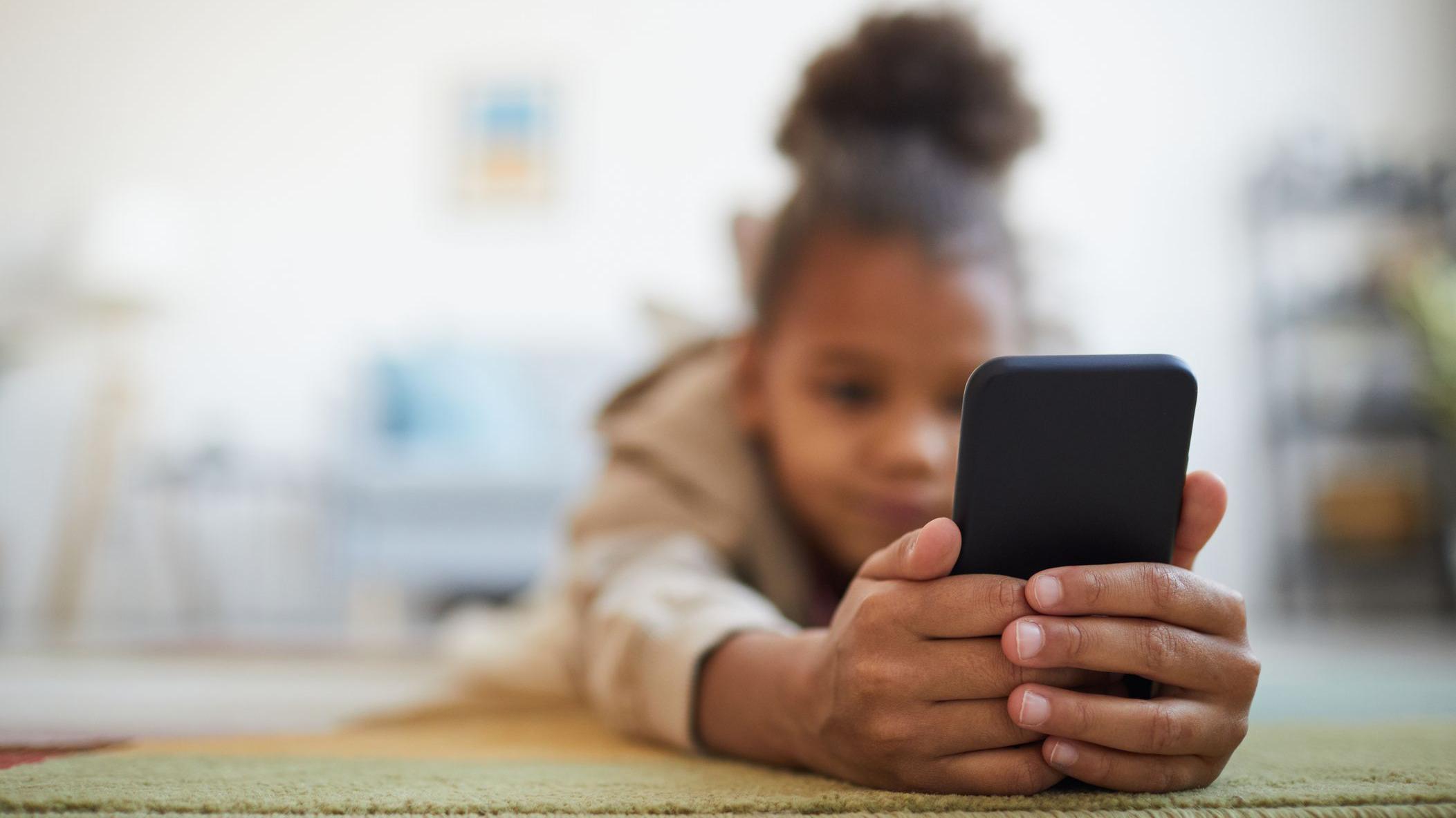 Close de uma menina segurando um smartphone enquanto est&aacute; deitada no ch&atilde;o 