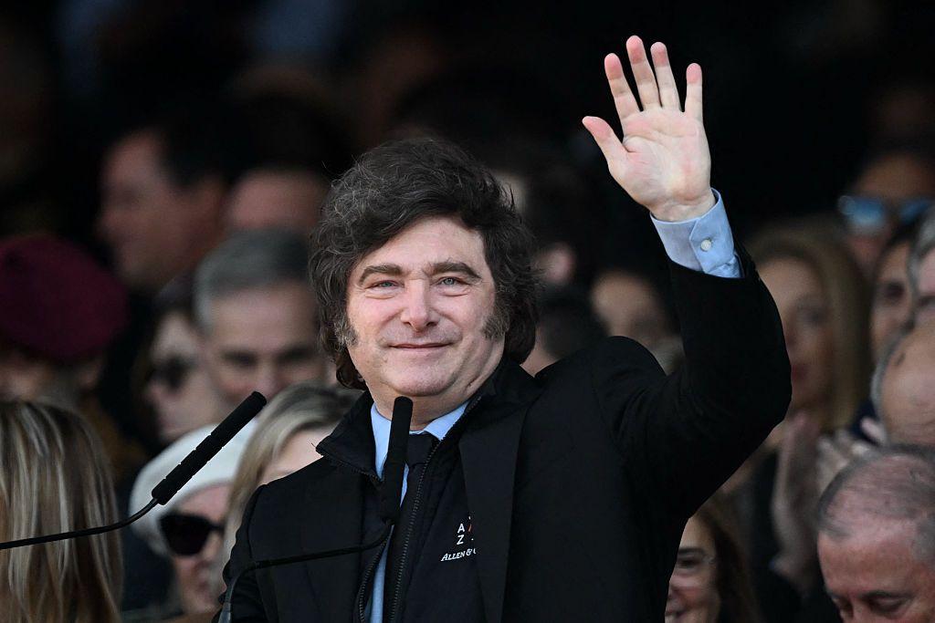 Javier Milei saludando con un traje oscuro y camisa color celeste.