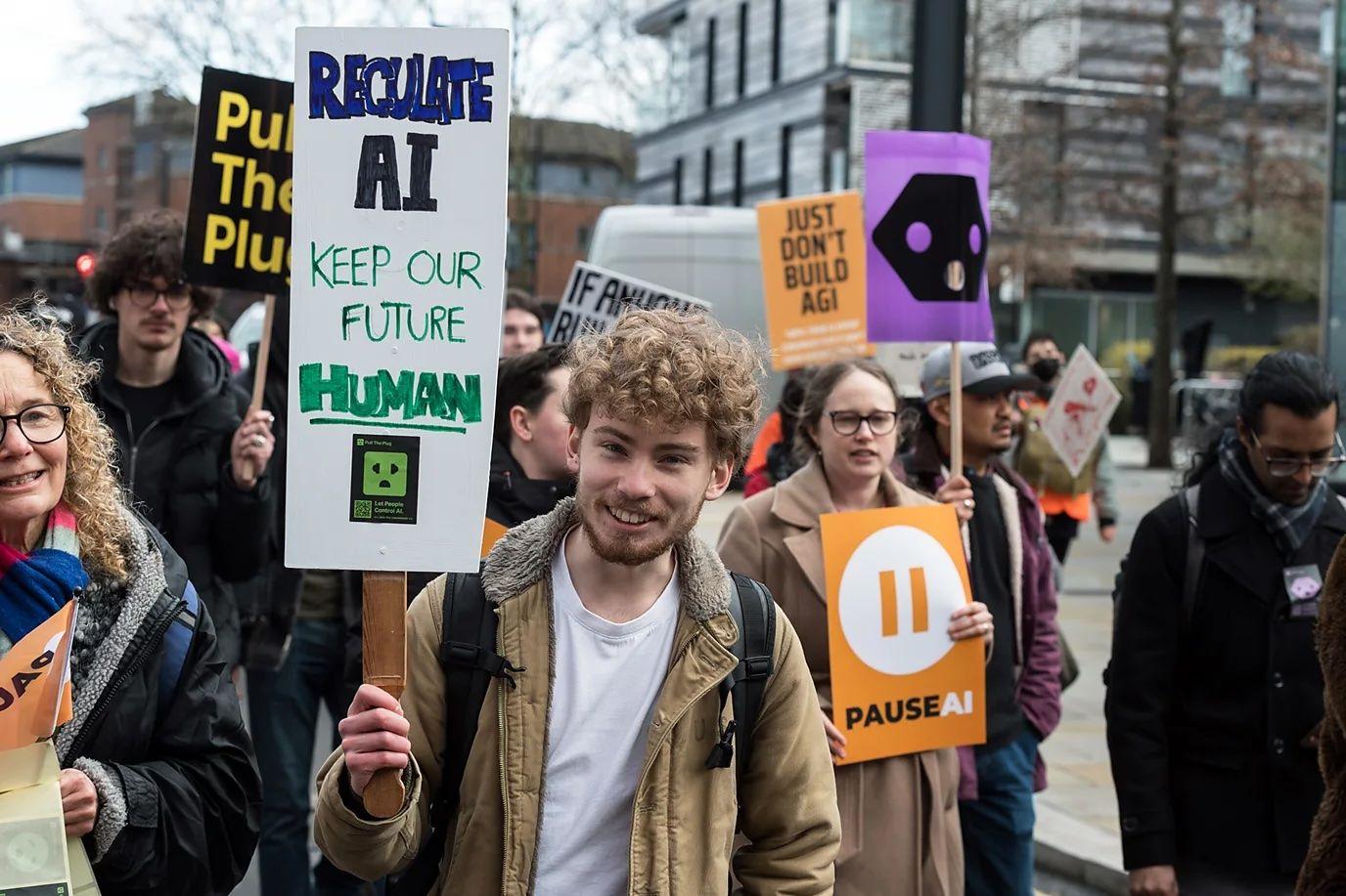 Un joven sonriente sostiene un cartel pidiendo que se regule la IA, para mantener un "futuro humano", en medio de una protesta. 