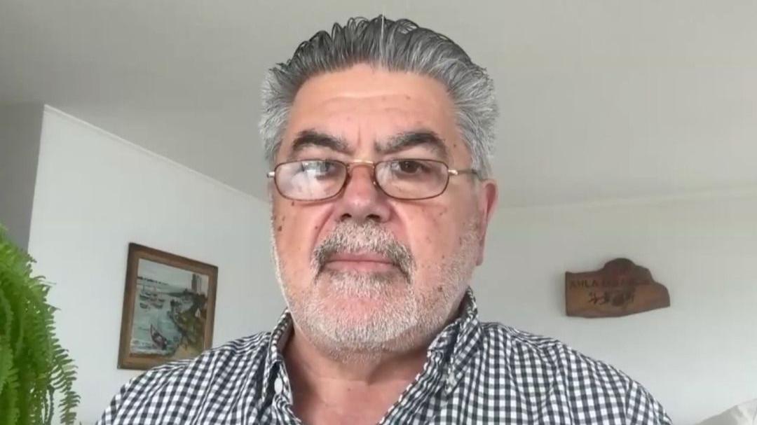 A mid-shot of Jorge Odón as he looks directly into the camera. He has short grey hair and is wearing glasses and a black and white checked shirt. 