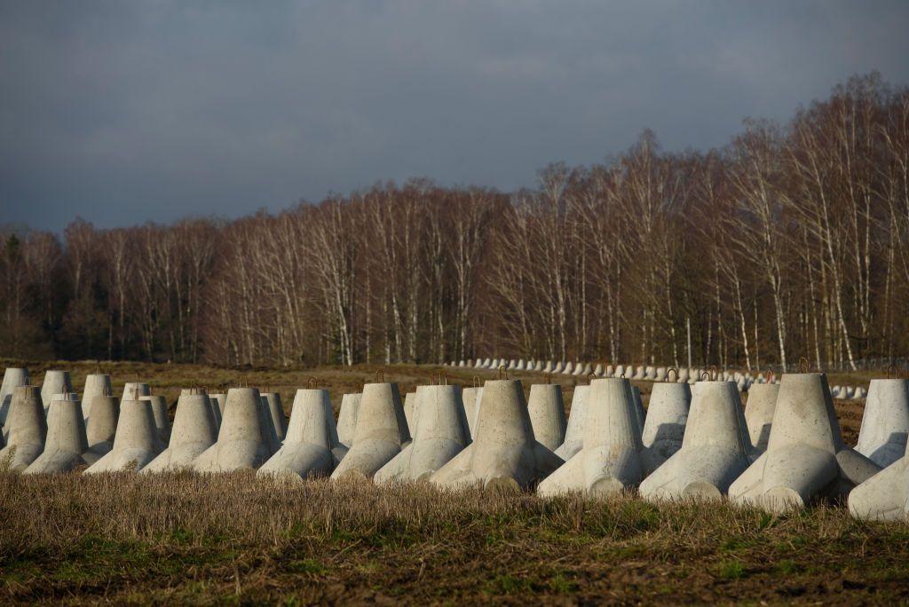 Una larga y densa fila de estructuras piramidales de concreto en un campo despejado bordea un bosque