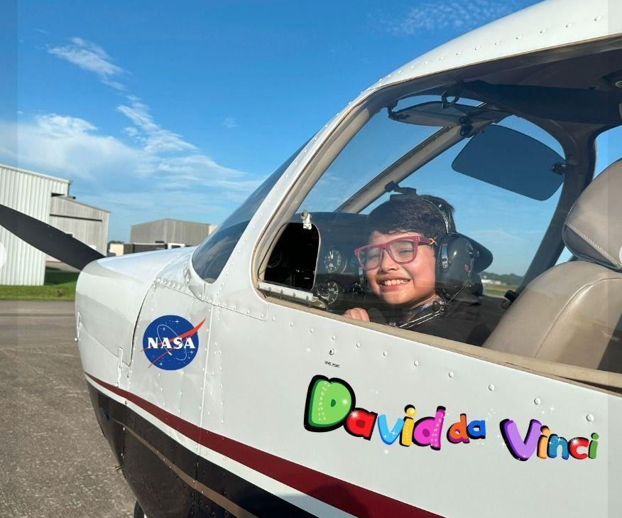 David en la cabina de una avioneta donde está impreso el nombre "David da Vinci" y un logo de la NASA.