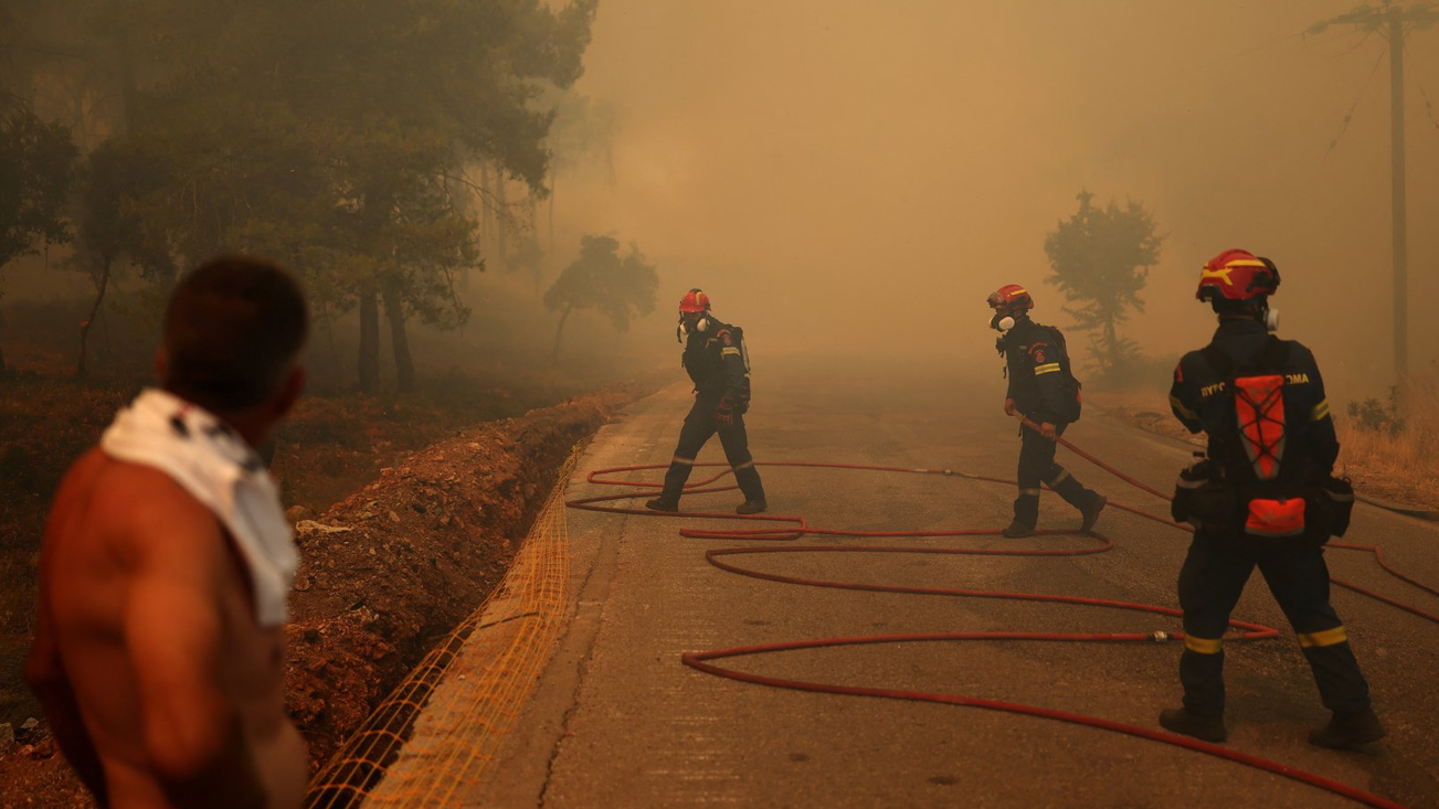 Vatrogasci prelaze cestu da gas epožar, muškarac gleda zadinljeno narandžasto nebo, ima majicu preko ramena