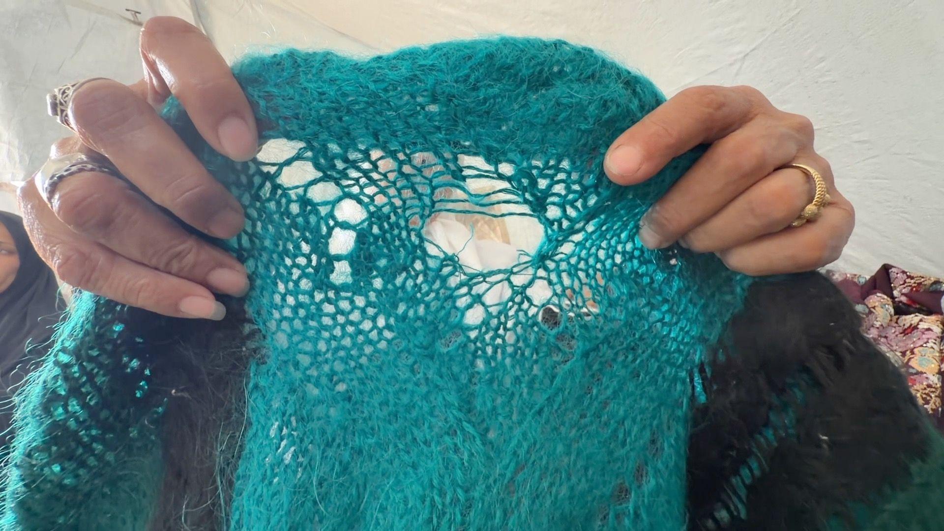 Os dedos com aneis de Amani Abu Salmiya exibem uma pe&ccedil;a de roupa azul tricotada com um buraco no centro.