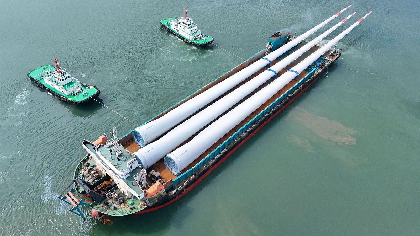 Dos remocadores estabilizan en el mar con ataduras a un gran barco que carga tres largas aspapas blancas puntudas