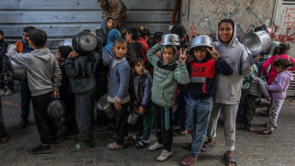 عدد من الأطفال الغزيين واقفين ضمن "طابور" ويحملون أواني.
