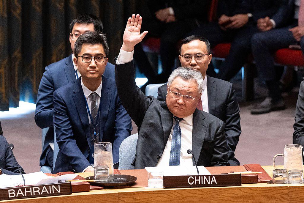 Un hombre levanta la mano en una mesa con el rótulo con la palabra china en el Consejo de Seguridad de Naciones Unidas. Detrás de él hay varios hombres y a su derecha se ve un rótulo con la palabra "Bahrain". 