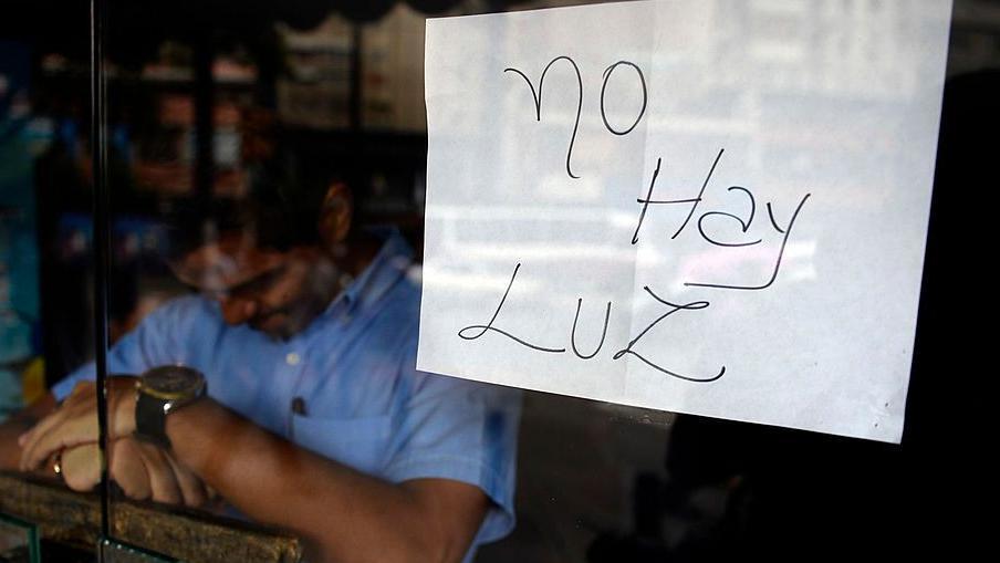 Un empleado de un negocio cerrado durante un apagón permanece detrás de la puerta con un letrero que dice: "No hay luz", en Caracas.